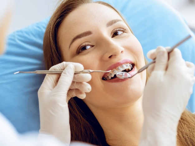 Mujer joven sonriente con soportes de ortodoncia examinados por dentista en clínica dental. Dientes sanos y concepto de medicina.