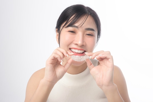 Mujer joven sonriente sosteniendo aparatos ortopédicos invisalign sobre fondo blanco estudio