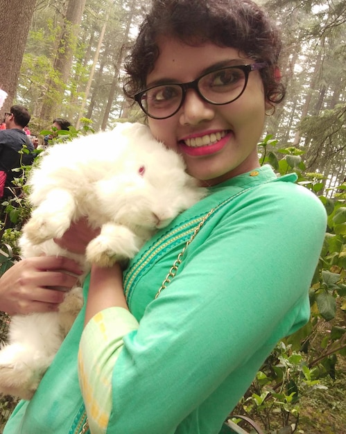 Foto mujer joven sonriente sosteniendo un conejo en el bosque