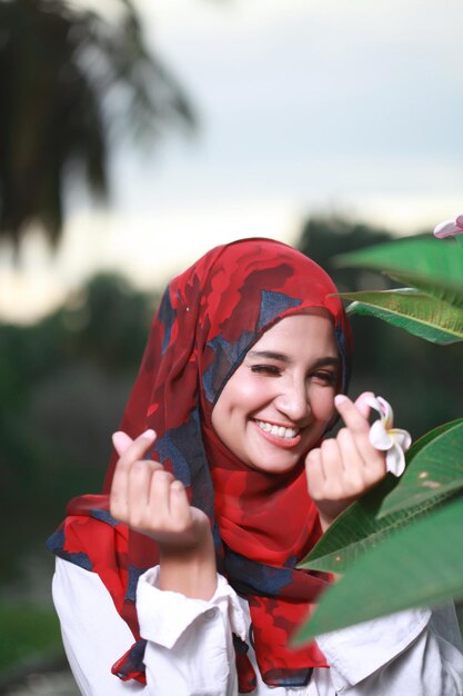 Foto mujer joven sonriente sosteniendo un frangipani junto a una planta en el parque durante la puesta de sol