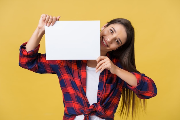 Mujer joven sonriente sosteniendo una hoja de papel blanco Retrato de estudio sobre fondo amarillo