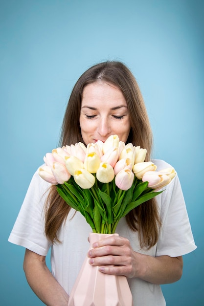 Mujer joven sonriente sosteniendo un ramo de tulipanes sobre fondo azul