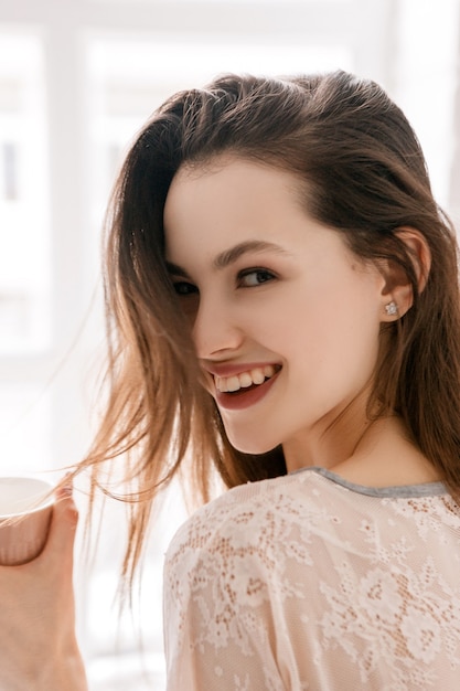 Mujer joven sonriente con una taza de café por la mañana. Publicidad de energía positiva