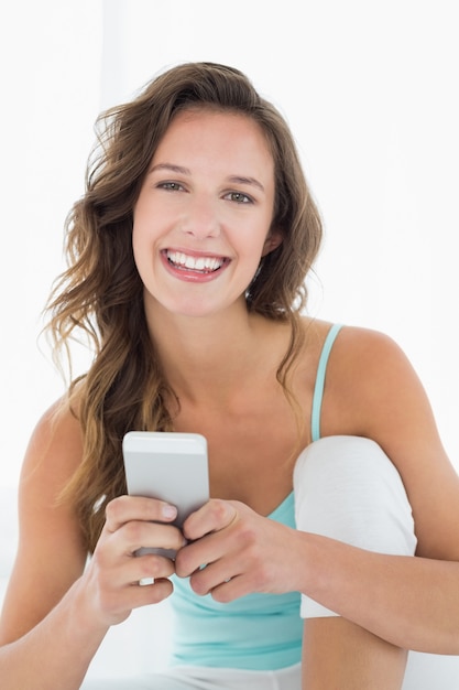 Mujer joven sonriente con el teléfono móvil en cama