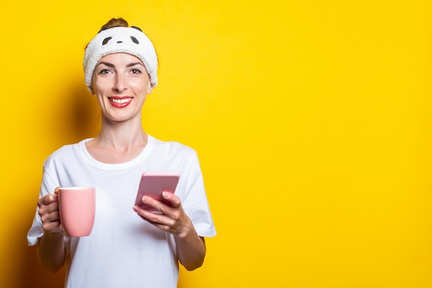 Mujer joven sonriente con un teléfono y una taza de café sobre un fondo amarillo