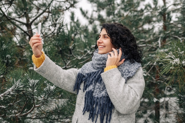 Foto mujer joven sonriente tomando selfie en el parque de invierno cubierto de nieve.