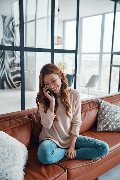 Foto mujer joven sonriente tomando el teléfono mientras está sentado en el sofá en casa