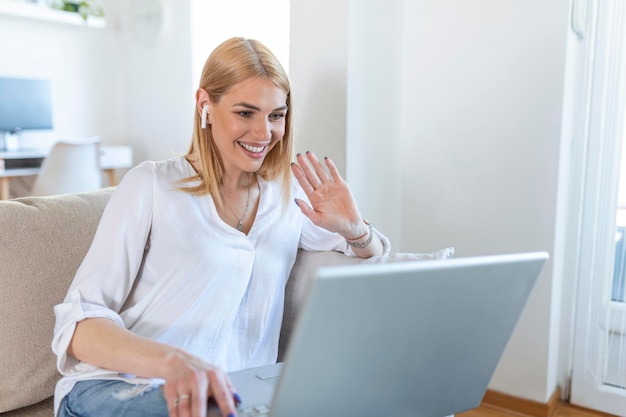 Foto mujer joven sonriente usando una computadora portátil en casa, mirando la pantalla, charlando, usando auriculares inalámbricos con videoconferencia. tutoría de formadores de negocios por cámara web, formación en línea, concepto de e-coaching