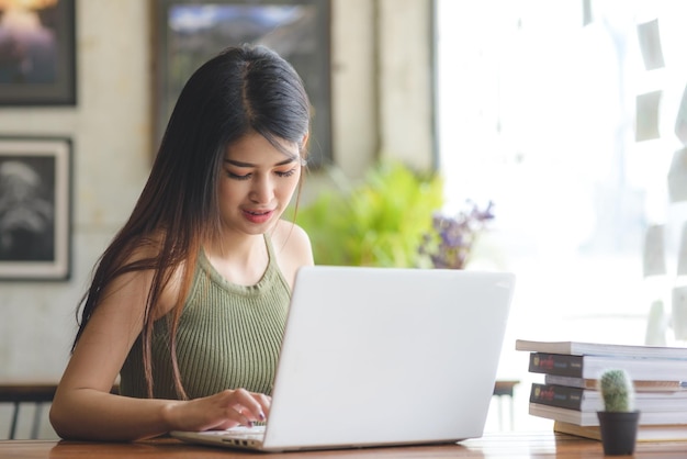 Mujer joven sonriente usando una computadora portátil mientras está sentada en la mesa