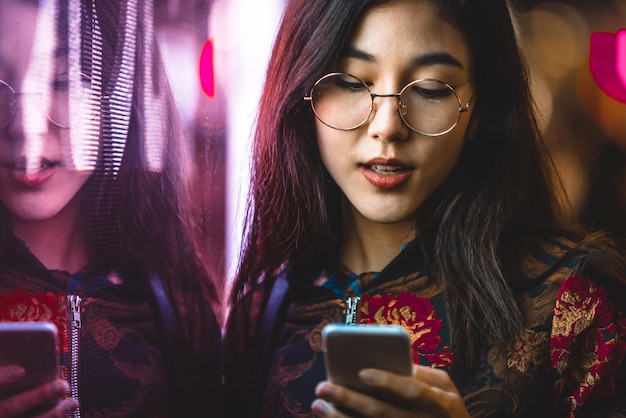 Mujer joven sonriente usando teléfono inteligente por la ventana con reflejo por la noche