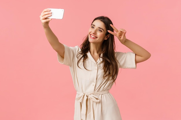 Foto mujer joven sonriente usando el teléfono mientras está de pie contra un fondo rosa