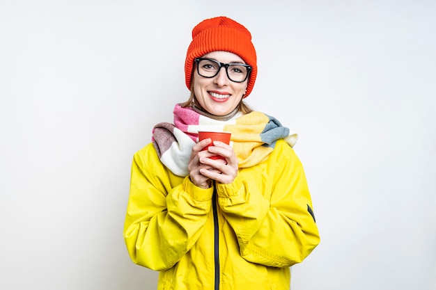 Mujer joven sonriente en vasos con una taza de papel sobre un fondo claro.