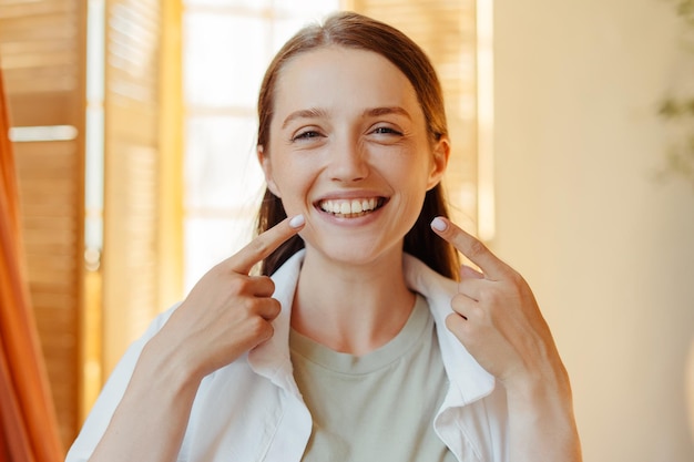 mujer joven con una sonrisa emocional de dientes apuntando con los dedos en la boca mirando a la cámara