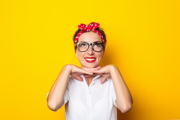 Mujer joven con una sonrisa, con gafas y una diadema roja en la cabeza sobre una pared amarilla.