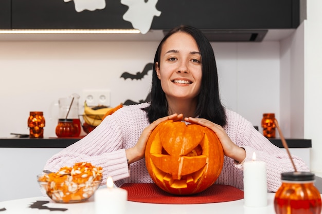 Mujer joven con una sonrisa mirando a la cámara y abrazando una calabaza para halloween