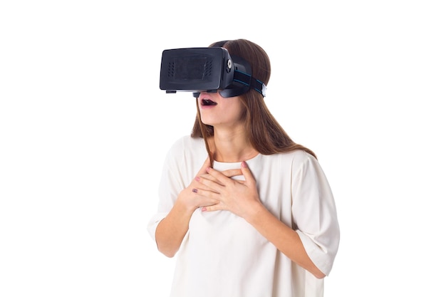 Mujer joven sorprendida con camisa blanca usando gafas de realidad virtual sobre fondo blanco en el estudio