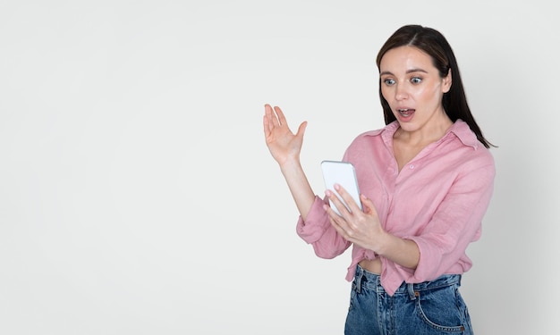 Mujer joven sorprendida mirando el teléfono inteligente y gesticulando