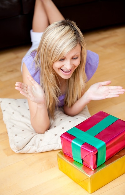 Mujer joven sorprendida que abre los regalos que mienten en el piso en la sala de estar