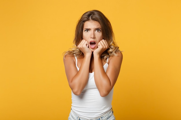 Mujer joven sorprendida con ropa informal ligera posando aislada en el fondo de la pared naranja amarilla en el estudio. Concepto de estilo de vida de las personas. Simulacros de espacio de copia. Mantener la boca abierta Apoyar las manos sobre la barbilla.