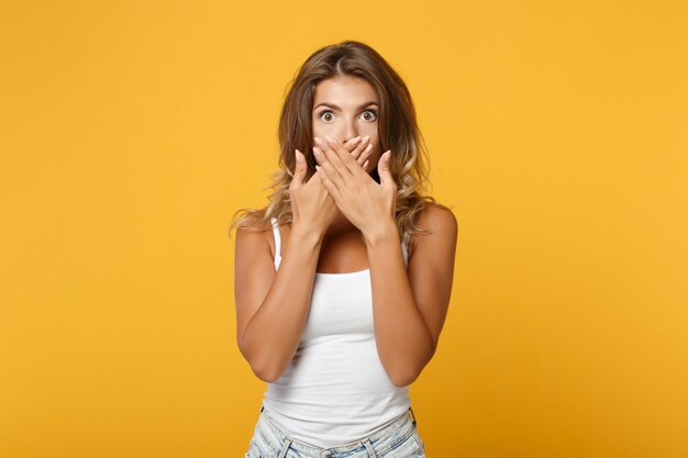 Mujer joven sorprendida con ropa informal ligera posando aislada en un retrato de estudio de fondo naranja amarillo. Gente emociones sinceras concepto de estilo de vida. Simulacros de espacio de copia. Cubrir la boca con las manos.