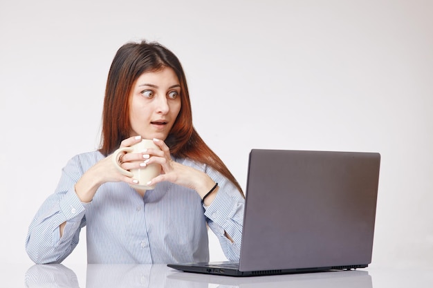 Mujer joven sorprendida sosteniendo una taza y mirando la computadora