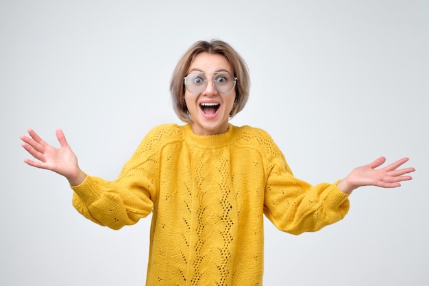 Mujer joven sorprendida en suéter amarillo gritando sorprendida con buenas noticias