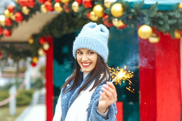 Mujer joven sorprendida viste abrigo azul disfrutando de las vacaciones con luces de bengala