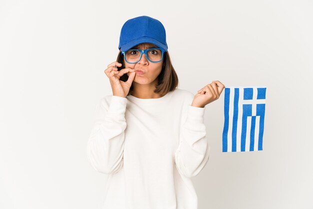 Mujer joven sosteniendo una bandera de Grecia con los dedos en los labios manteniendo un secreto