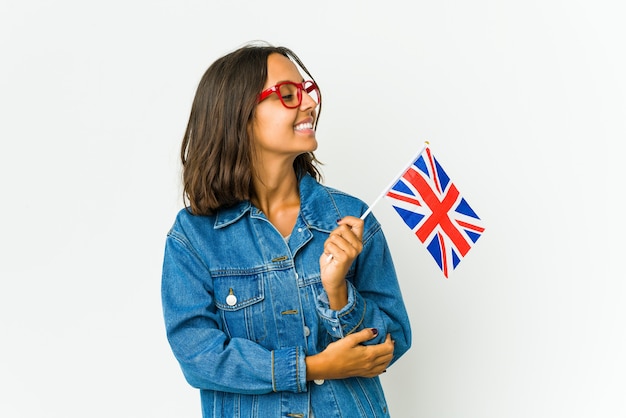 Mujer joven sosteniendo una bandera inglesa aislada en la pared blanca sonriendo confiado con los brazos cruzados