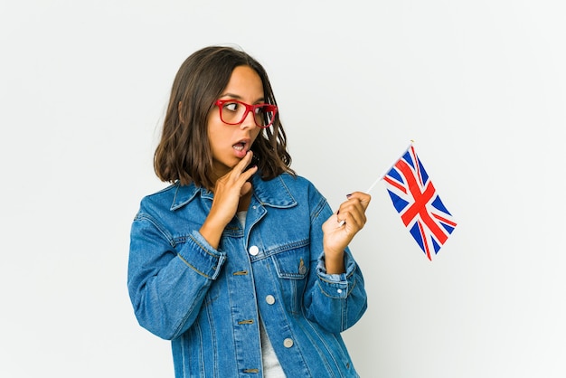 Mujer joven sosteniendo una bandera inglesa aislada en la pared blanca sorprendida por algo que ha visto