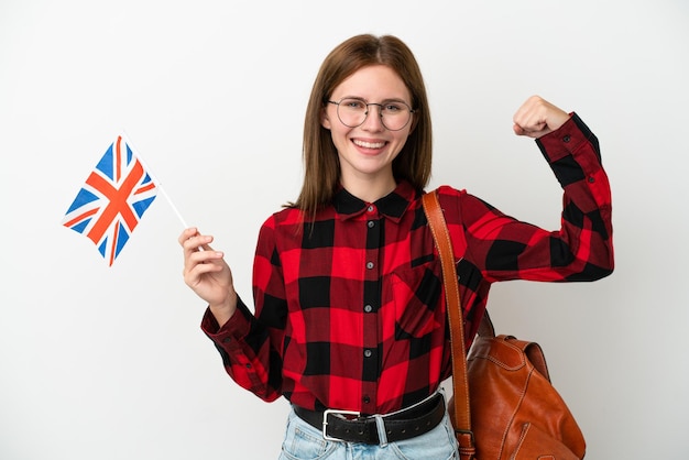 Mujer joven sosteniendo una bandera del Reino Unido aislada de fondo azul haciendo un gesto fuerte