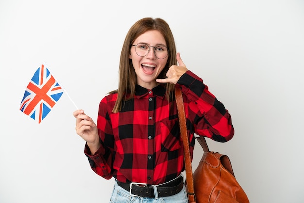 Mujer joven sosteniendo una bandera del Reino Unido aislada en un fondo azul haciendo un gesto telefónico Llámame de nuevo