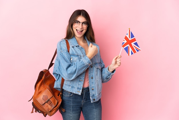 Mujer joven sosteniendo una bandera del Reino Unido aislada en la pared rosa celebrando una victoria