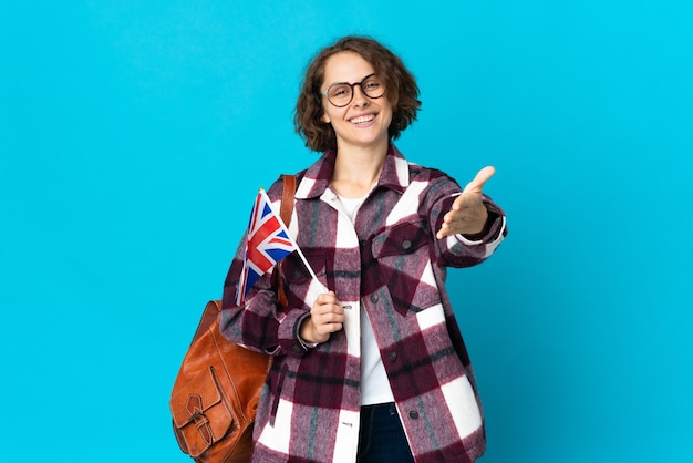 Mujer joven sosteniendo una bandera del Reino Unido aislado un apretón de manos para cerrar un buen trato