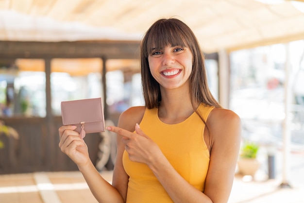 Mujer joven sosteniendo una billetera al aire libre y apuntándola