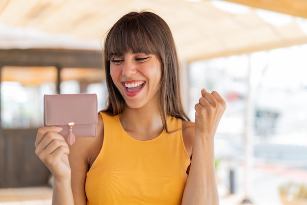 Foto mujer joven sosteniendo una billetera al aire libre celebrando una victoria
