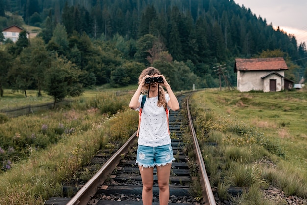 mujer joven sosteniendo binoculares, chica turista con mochila de vista del paisaje de la antigua estación de tren.