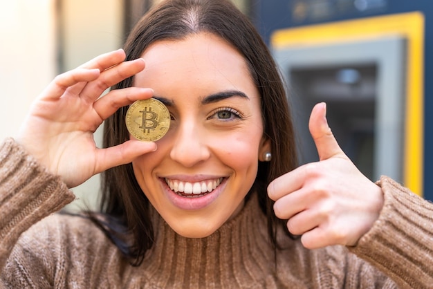 Mujer joven sosteniendo un Bitcoin al aire libre