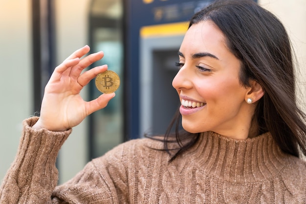 Mujer joven sosteniendo un Bitcoin al aire libre