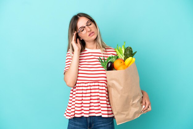 Mujer joven sosteniendo una bolsa de compras aislada de fondo azul con dolor de cabeza