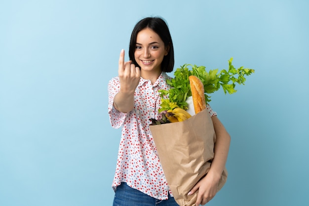 Mujer joven sosteniendo una bolsa de compras haciendo el gesto que viene