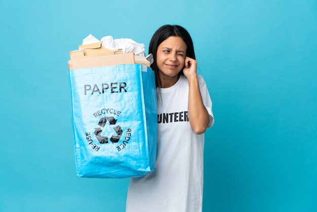 Mujer joven sosteniendo una bolsa de reciclaje llena de papel frustrado y cubriendo las orejas