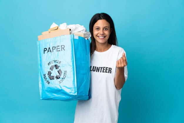 Mujer joven sosteniendo una bolsa de reciclaje llena de papel haciendo gesto de dinero