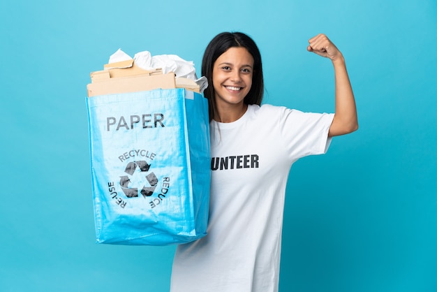 Mujer joven sosteniendo una bolsa de reciclaje llena de papel haciendo un gesto fuerte