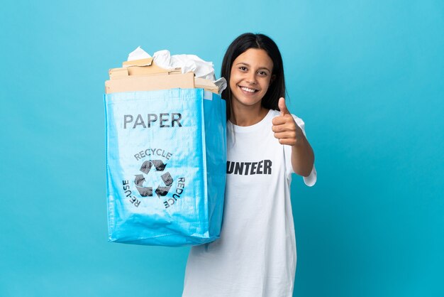 Mujer joven sosteniendo una bolsa de reciclaje llena de papel con los pulgares hacia arriba porque ha sucedido algo bueno