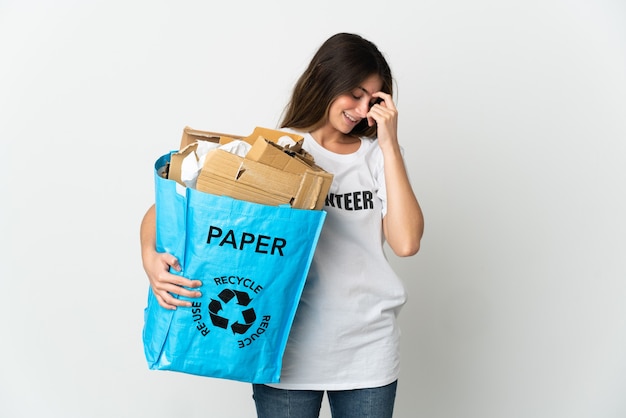 Mujer joven sosteniendo una bolsa de reciclaje llena de papel para reciclar aislado en blanco riendo