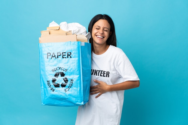 Mujer joven sosteniendo una bolsa de reciclaje llena de papel sonriendo mucho