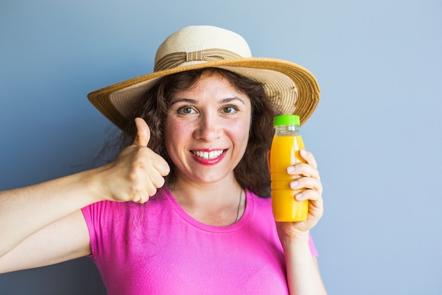 Mujer joven sosteniendo una botella con jugo y mostrando los pulgares para arriba gesto.