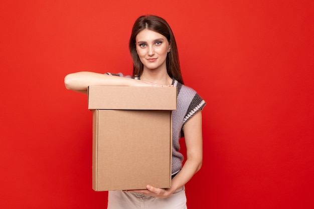 Mujer joven sosteniendo cajas de cartón en la pared roja