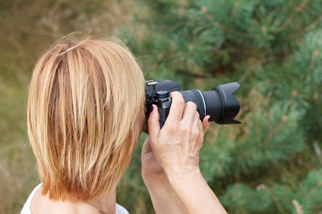 Mujer joven sosteniendo una cámara digital y tomando fotografías del paisaje de verano en el bosque